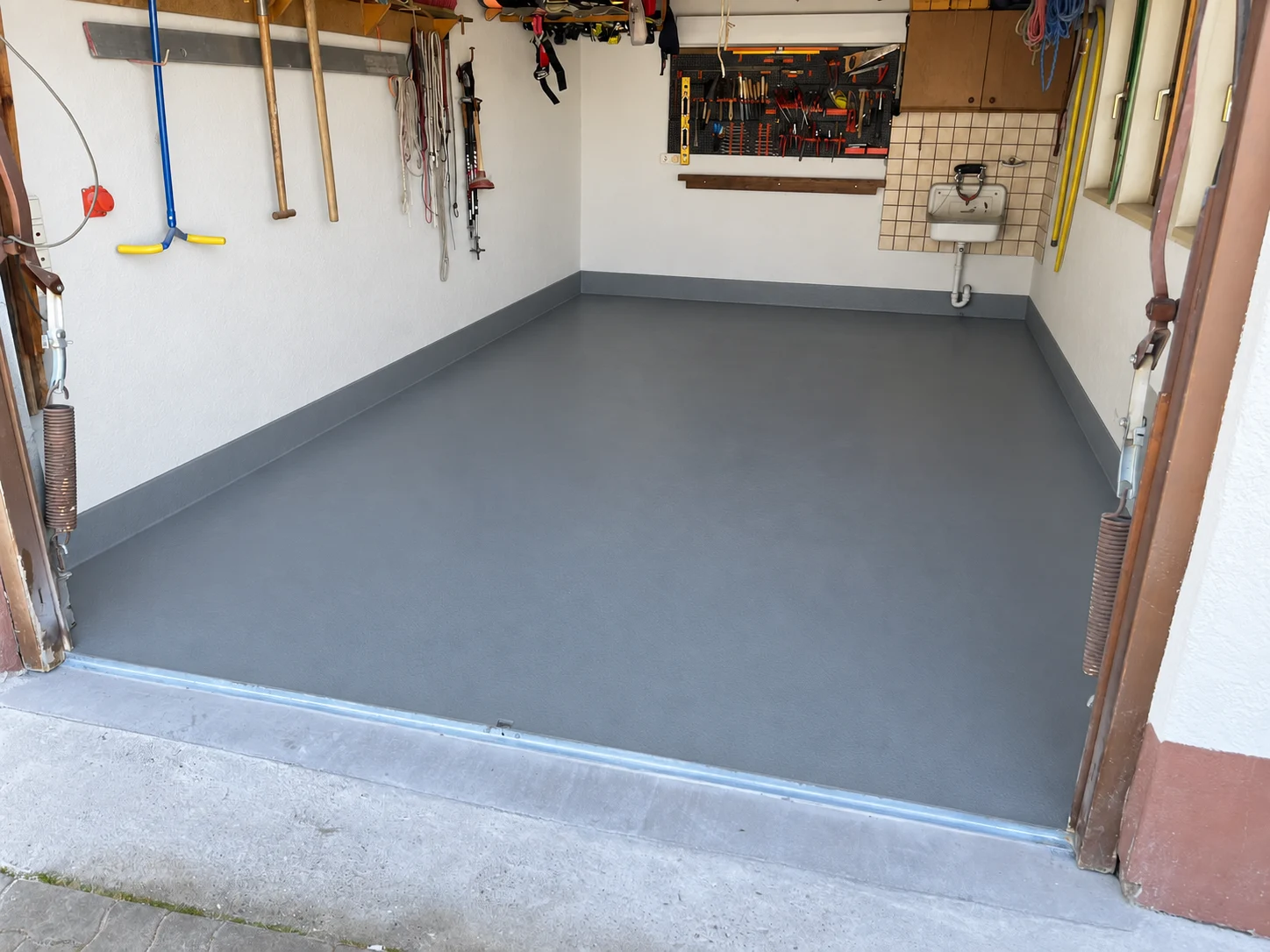 Garage mit gleichmäßig grauer Bodenbeschichtung und umlaufendem Sockel