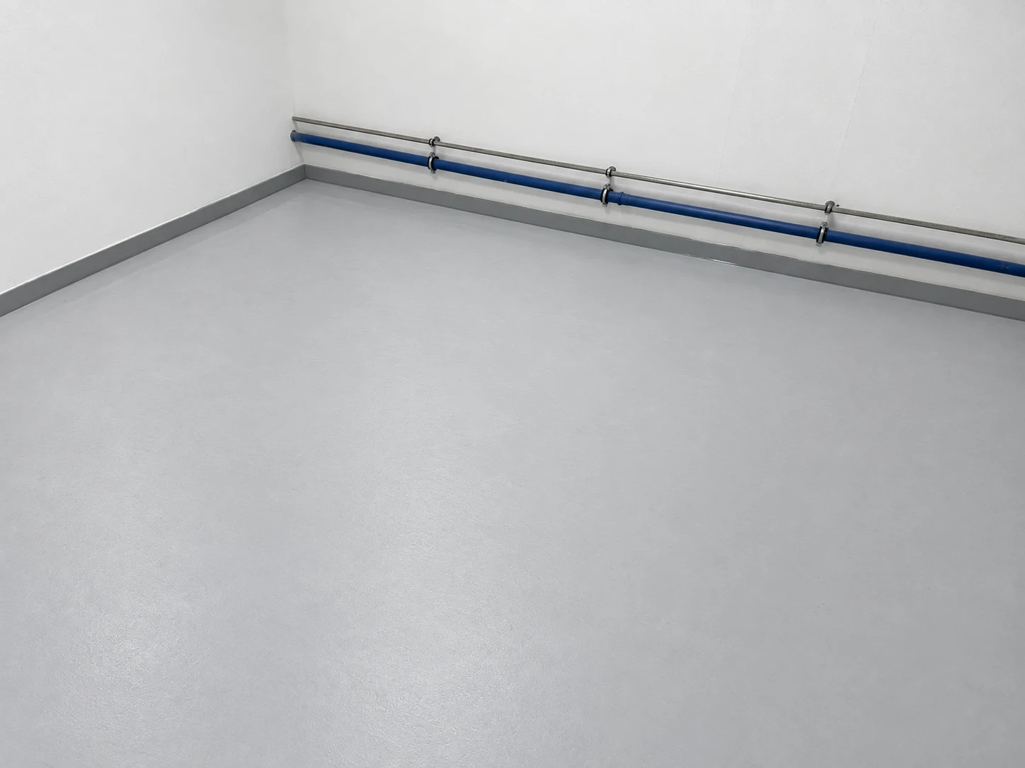 Hellgraue Bodenbeschichtung mit grauem Sockel und Wandanschluss in einem Funktionsraum