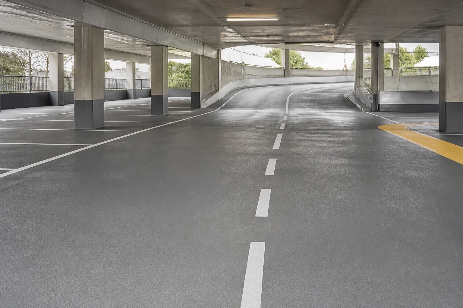Beschichtete Fahrspur mit Stellflächen und Rampe in einem offenen Parkhaus